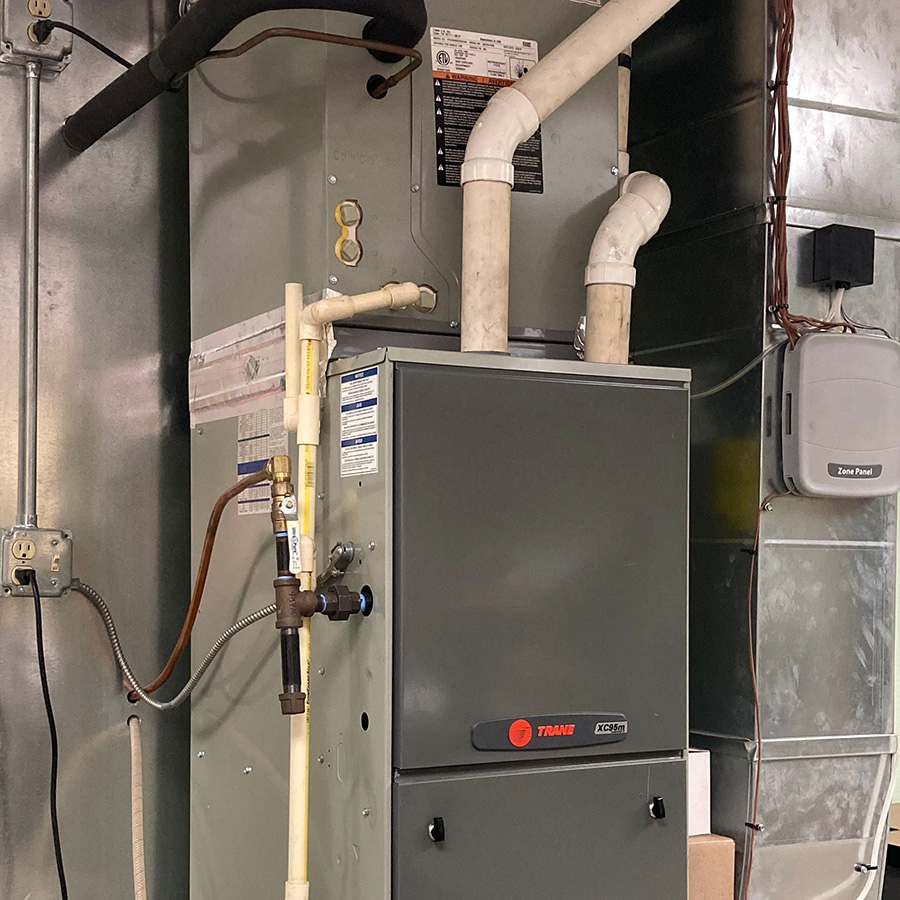 Indoor Trane furnace and HVAC system installed with connected ductwork, pipes, and control components.